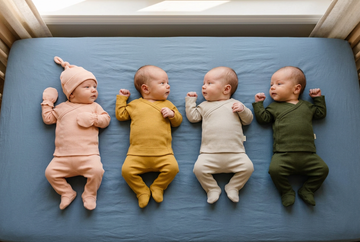 Vier newborn baby’s naast elkaar in de vierdelige sets in perzikroze, mosterd, lichtbeige en olijfgroen, met bijpassende mutsjes en handschoentjes