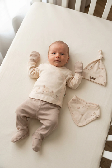 Newborn baby in beige overslaghemdje met schaapjes, broekje met voetjes en wantjes, met mutsje en slabbetje ernaast